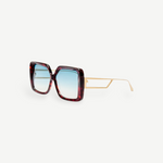 The Macy Sunglasses feature oversized square frames crafted from red tortoiseshell acetate, paired with thin gold arms and aqua gradient lenses, displayed on a white background.