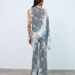 Wearing the Luma Trouser, which features a bold black-and-white zebra print, a person stands facing away against a plain white wall and concrete floor.