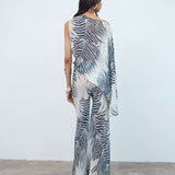 Wearing the Luma Trouser, which features a bold black-and-white zebra print, a person stands facing away against a plain white wall and concrete floor.