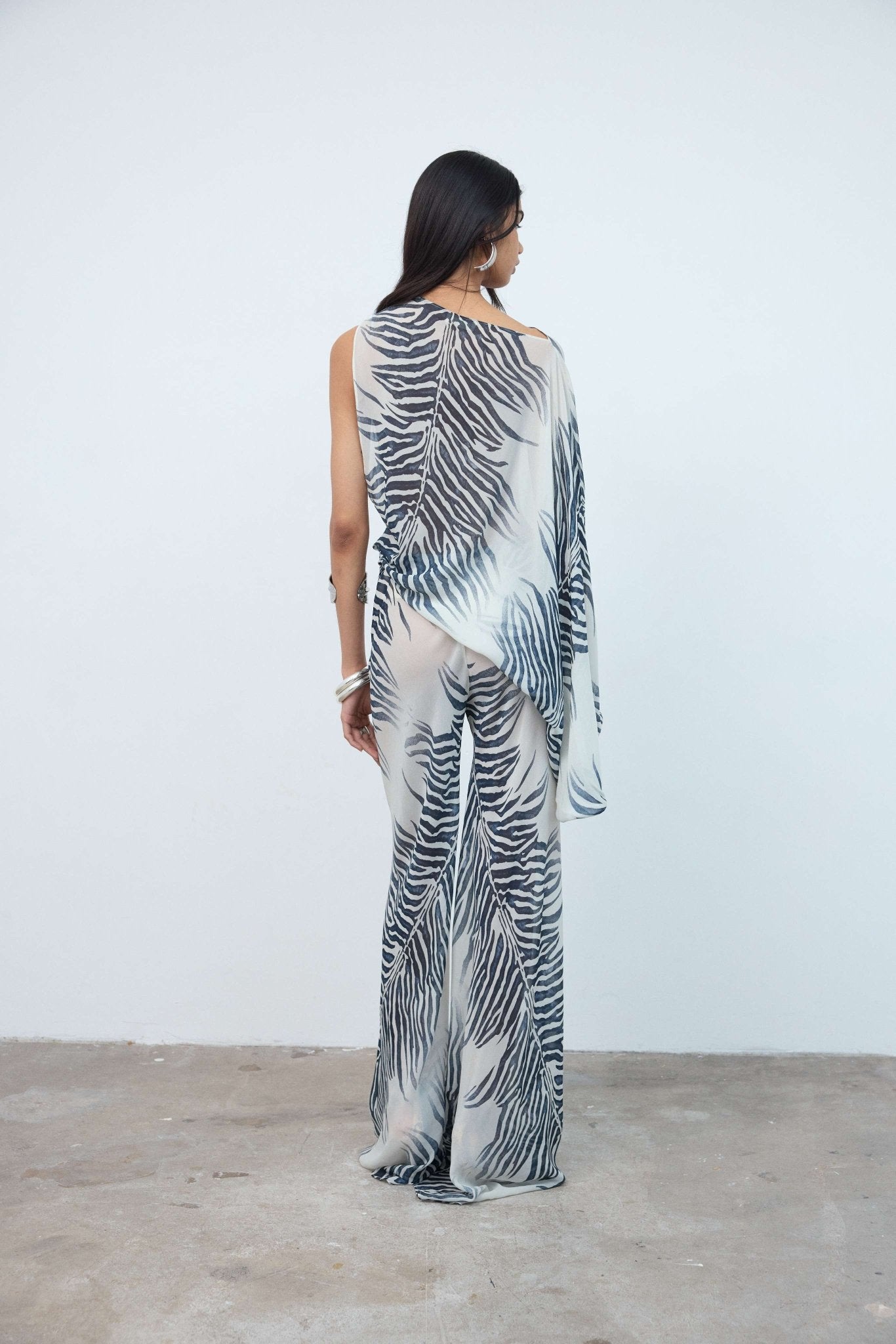 Wearing the Luma Trouser, which features a bold black-and-white zebra print, a person stands facing away against a plain white wall and concrete floor.