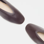 Two Luna Slipper Shoes in dark brown leather with rounded square toes and refined leather detailing, positioned diagonally on a white background.