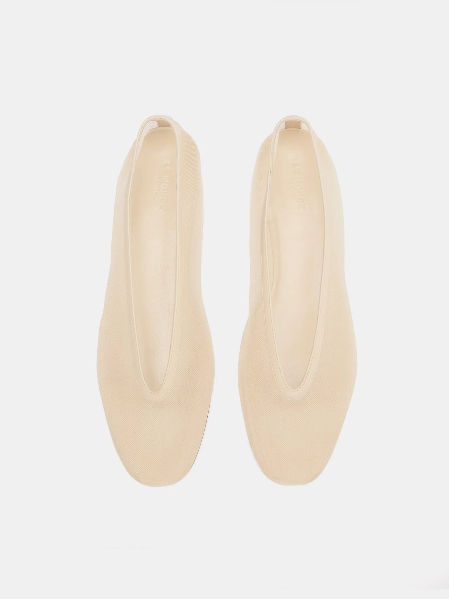 A pair of beige, minimalist Luna Slipper Shoes made from patent leather with an elongated oval opening is displayed on a white background, viewed from above.