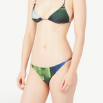 A person models the Dolores Top Classic Swimwear bikini with jewelry straps in green and blue, standing against a plain white background. The image is cropped from the shoulders down, and their face is not shown.
