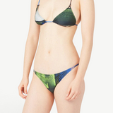 A person models the Dolores Top Classic Swimwear bikini with jewelry straps in green and blue, standing against a plain white background. The image is cropped from the shoulders down, and their face is not shown.