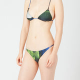 A person models the Dolores Top Classic Swimwear bikini with jewelry straps in green and blue, standing against a plain white background. The image is cropped from the shoulders down, and their face is not shown.