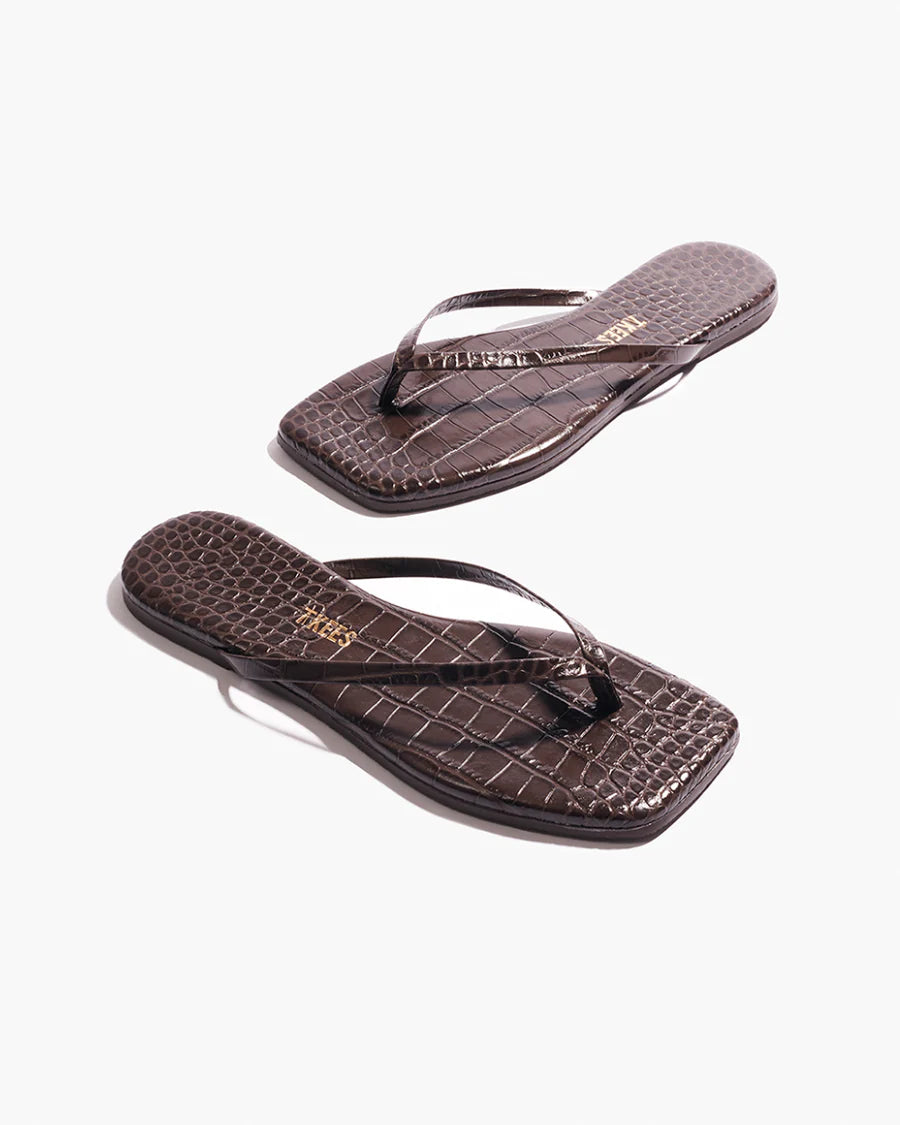A pair of Square Toe Lily, dark brown crocodile-embossed leather flip-flops with square toes are placed on a white background.