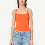 A woman wears a bright orange cotton-modal Duke Tank with a square neckline and blue denim shorts, styled for everyday wear.