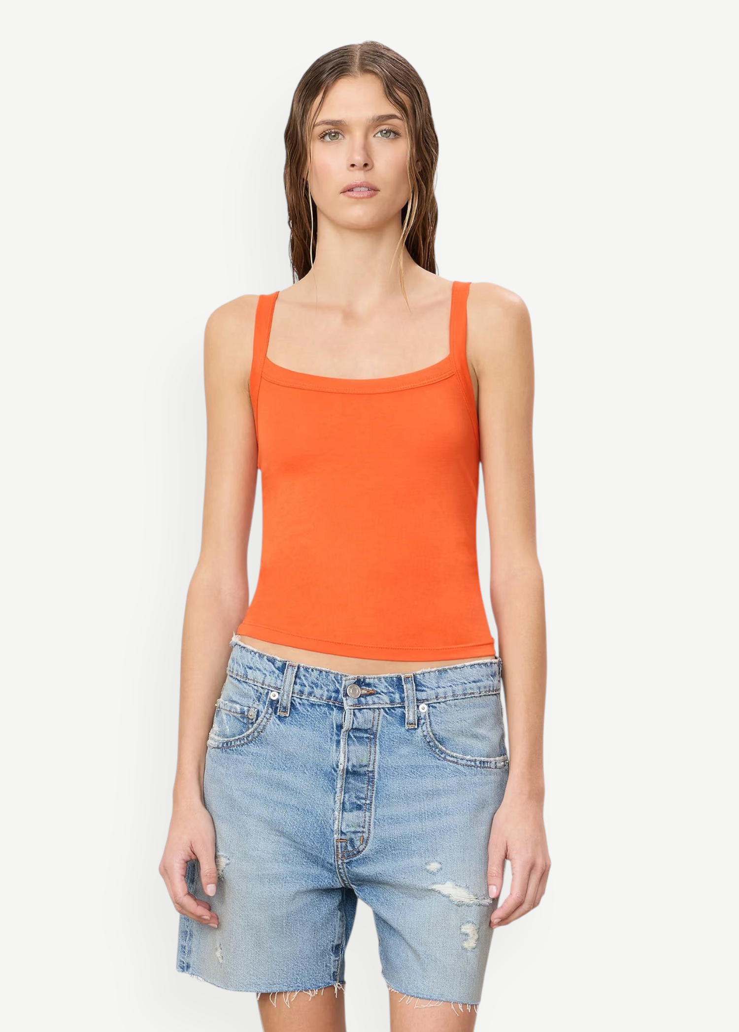A woman wears a bright orange cotton-modal Duke Tank with a square neckline and blue denim shorts, styled for everyday wear.