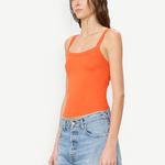 Woman wearing a bright orange, slim fit cotton-modal Duke Tank and light-wash denim shorts.