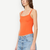 Woman wearing a bright orange, slim fit cotton-modal Duke Tank and light-wash denim shorts.