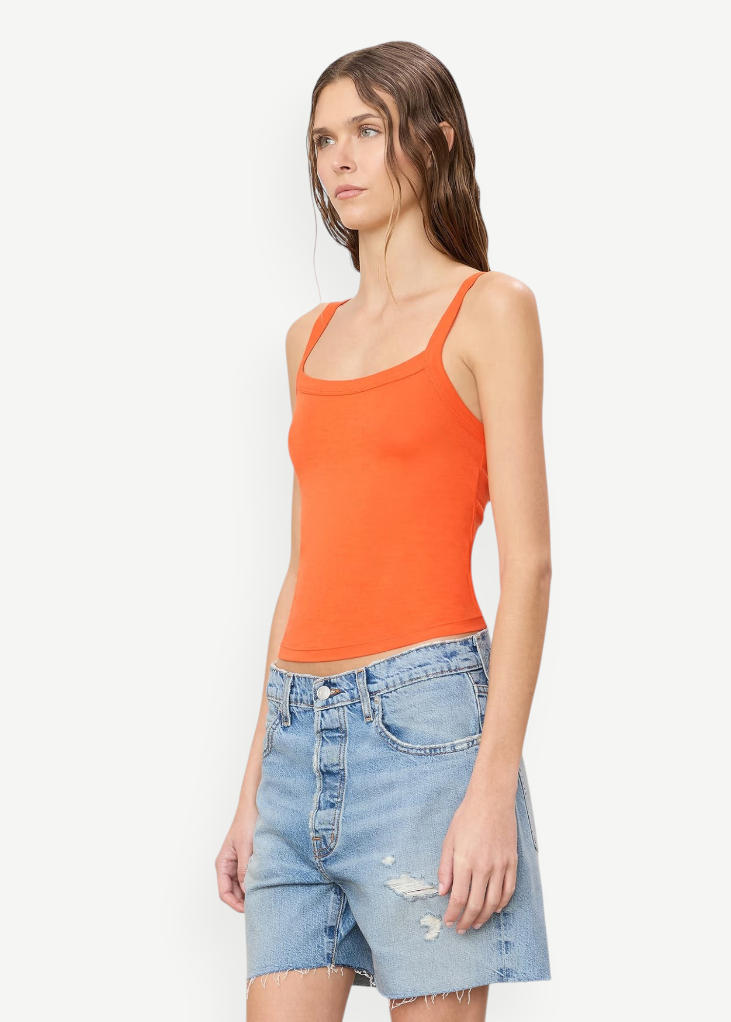 Woman wearing a bright orange, slim fit cotton-modal Duke Tank and light-wash denim shorts.