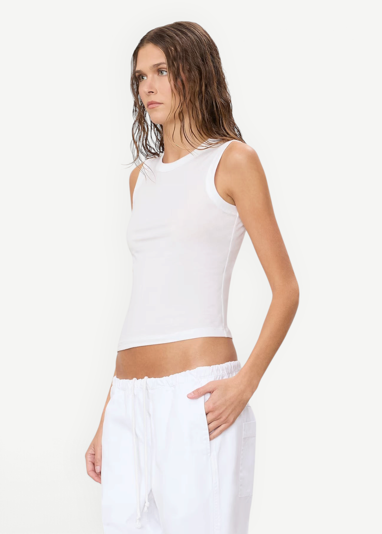 A person wears a white, slim-fit Fitted Muscle Tank paired with white drawstring pants.