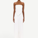 A person stands against a white background wearing The Triangle Top—a strapless piece with a pointed hem—paired with wide-leg white pants. This ensemble reflects the artistry of handmade clothing and an appreciation for sustainable fashion, while transparent glasses complete the effortlessly modern look.