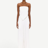 A person stands against a white background wearing The Triangle Top—a strapless piece with a pointed hem—paired with wide-leg white pants. This ensemble reflects the artistry of handmade clothing and an appreciation for sustainable fashion, while transparent glasses complete the effortlessly modern look.