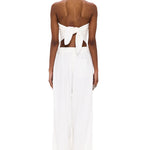 A person stands facing away, wearing The Triangle Top—a white strapless piece tied in a bow at the back—paired with wide-leg white pants featuring an elastic waistband. Handcrafted to embody sustainable fashion ideals, this minimalist ensemble is elevated by Moroccan weaving influences, celebrating the artistry of handmade clothing against a plain white background.
