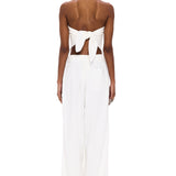 A person stands facing away, wearing The Triangle Top—a white strapless piece tied in a bow at the back—paired with wide-leg white pants featuring an elastic waistband. Handcrafted to embody sustainable fashion ideals, this minimalist ensemble is elevated by Moroccan weaving influences, celebrating the artistry of handmade clothing against a plain white background.
