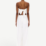 A person stands facing away, wearing The Triangle Top—a white strapless piece tied in a bow at the back—paired with wide-leg white pants featuring an elastic waistband. Handcrafted to embody sustainable fashion ideals, this minimalist ensemble is elevated by Moroccan weaving influences, celebrating the artistry of handmade clothing against a plain white background.