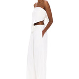 A person stands against a white background, wearing The Triangle Top—a white, strapless piece paired with loose white pants and clear glasses. With hands in their pockets and a confident gaze toward the camera, their outfit embodies sustainable fashion through handmade clothing inspired by Moroccan weaving traditions.