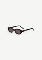 Certainly! Here’s a rewritten version using your product data: The Sylvie sunglasses feature black, oval-shaped frames with dark lenses and bold, thick sides adorned with LU—GOLDIE in gold lettering on the left arm, all showcased against a crisp white background—a true pocket rocket accessory that complements any vintage suit.