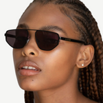Wearing the Victoire aviator sunglasses with UV400 protection and stud earrings, a person with braided hair gazes slightly upward against a plain background.