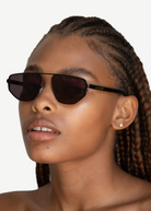 Wearing the Victoire aviator sunglasses with UV400 protection and stud earrings, a person with braided hair gazes slightly upward against a plain background.