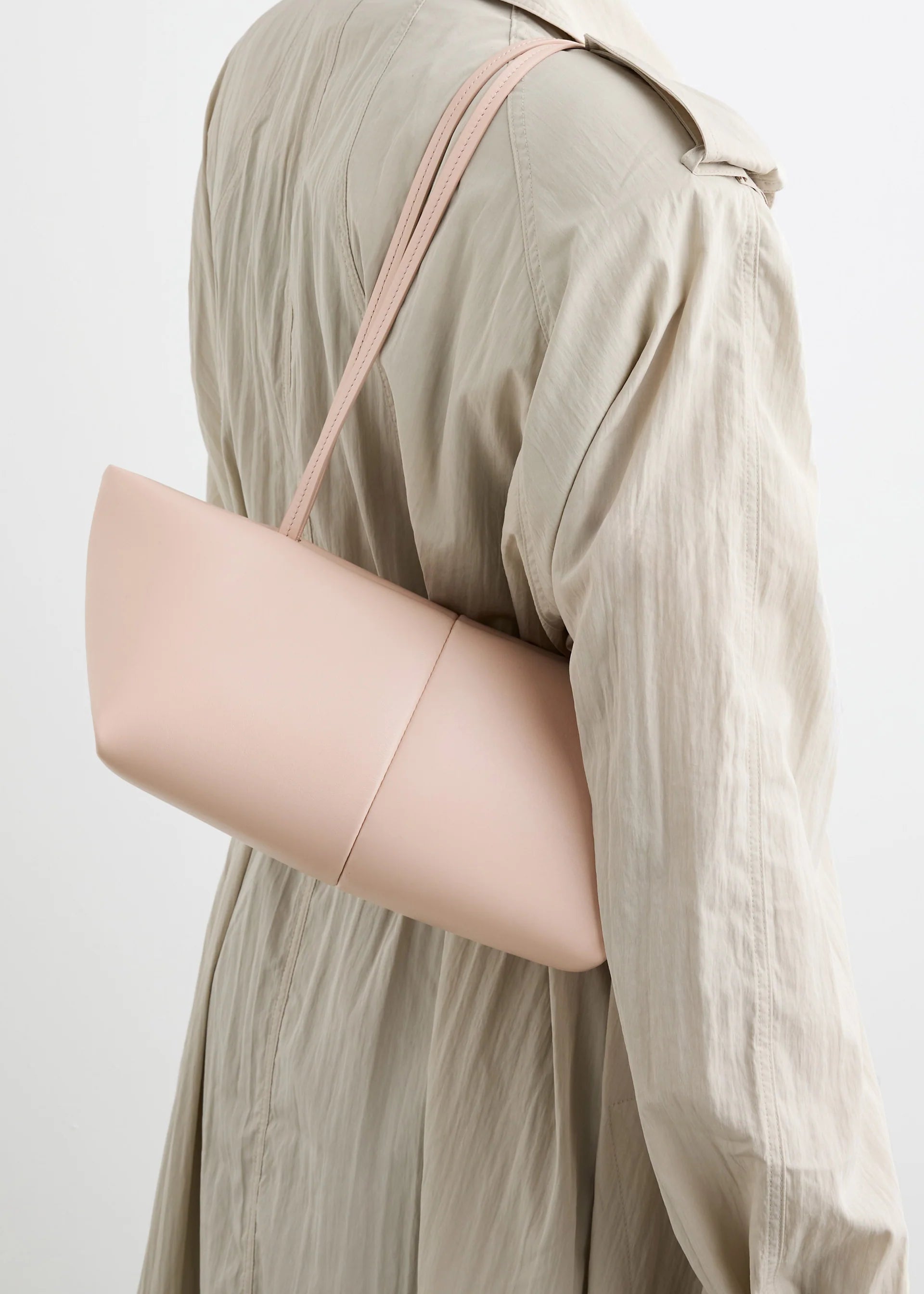 A person is shown from the back against a plain white background, wearing a beige trench coat and carrying the Boulevard Sling Bag in pale pink nappa leather over their shoulder.