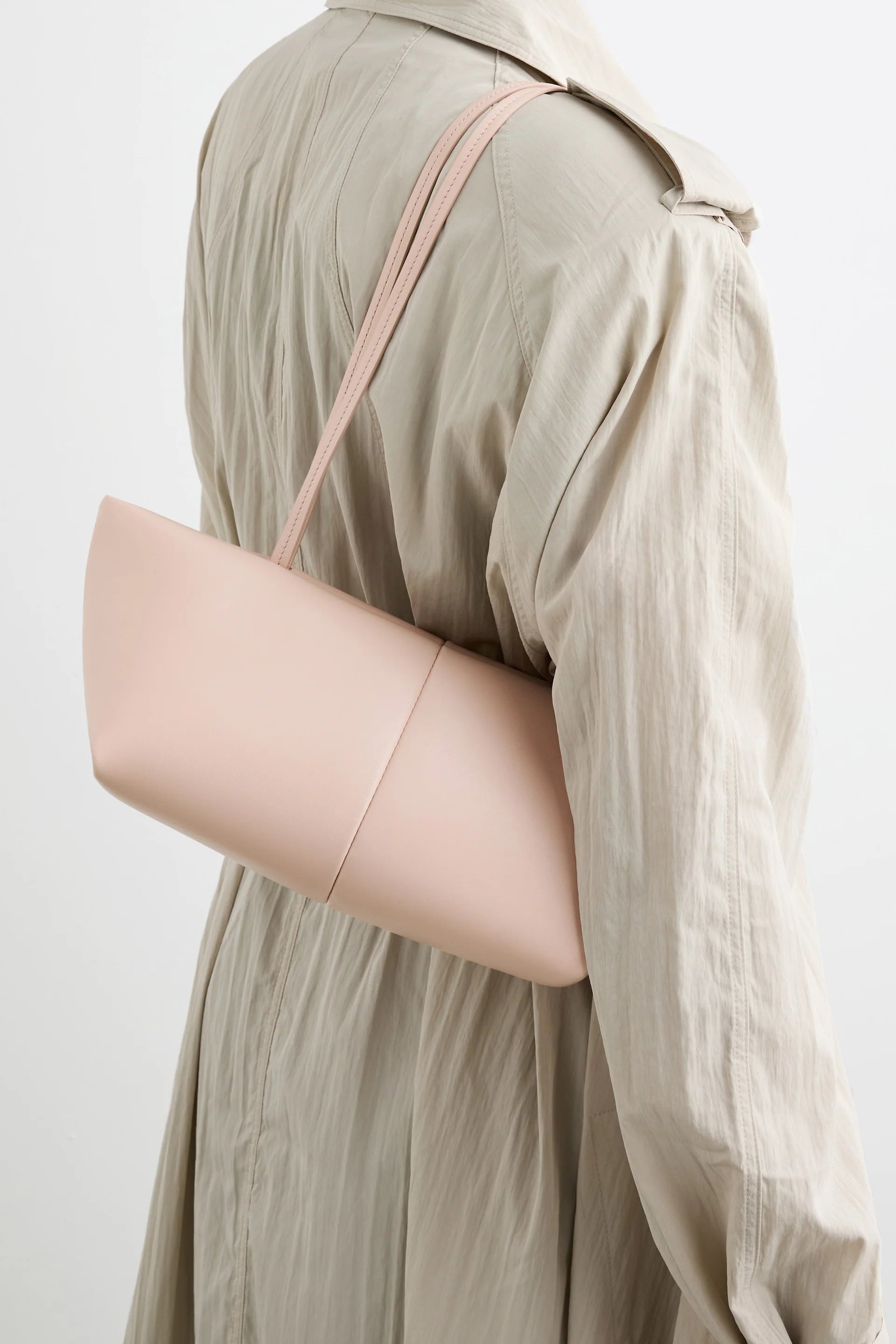 A person is shown from the back against a plain white background, wearing a beige trench coat and carrying the Boulevard Sling Bag in pale pink nappa leather over their shoulder.