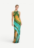 Model wearing KABE SHOP INC Magdalena long silk maxi dress with halter neckline and landscape print in green and gold