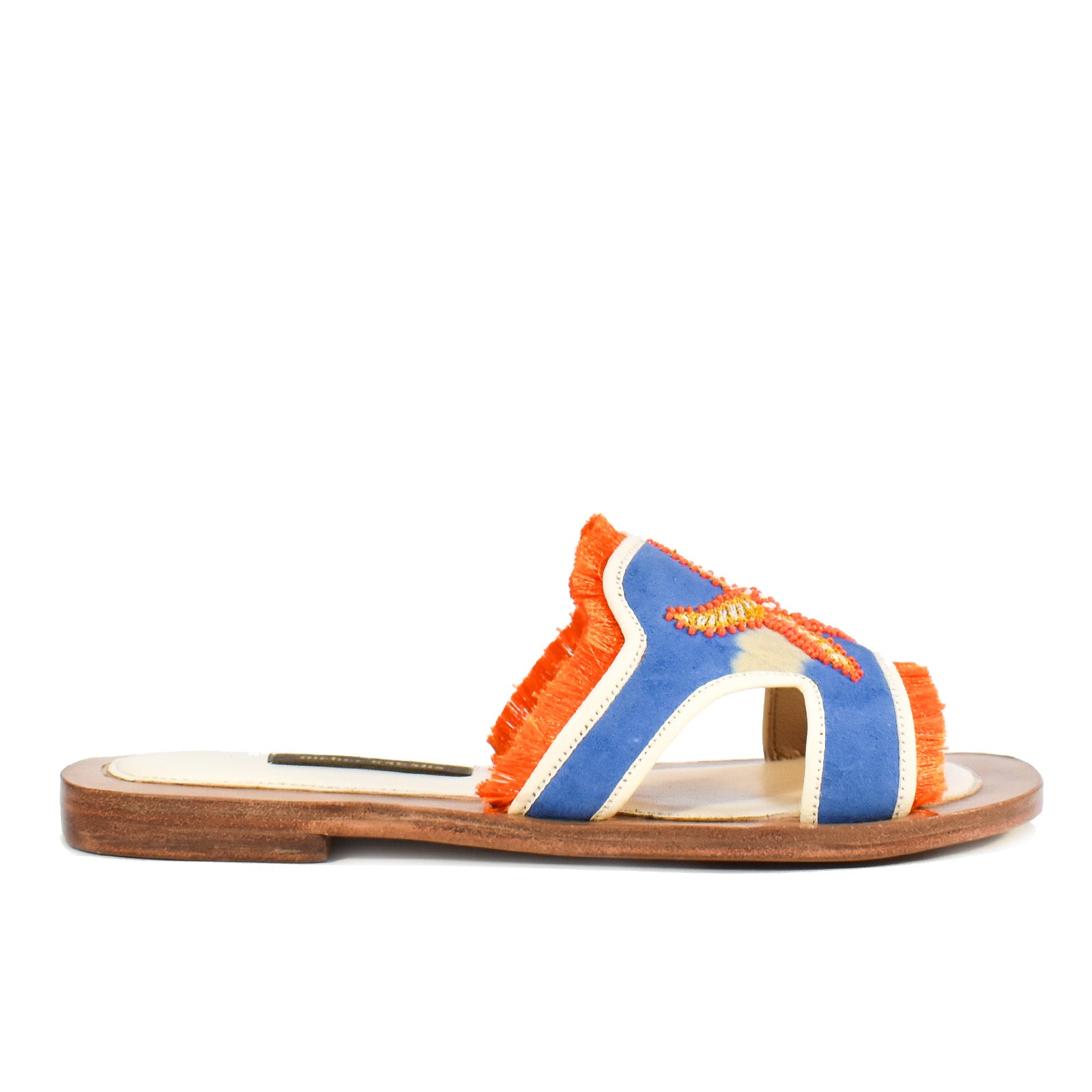 Introducing the Mazu Slide: these hand-embroidered leather slides feature a flat wooden sole, blue and orange fringe straps, and an intricate yellow and orange embroidered star detail on top. Inspired by Silk Route artisan shoes, the Mazu Slide offers a unique bohemian flair to any look.