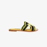 Introducing the Mazu Slide: a sustainable flat sandal featuring a wooden sole, yellow footbed, dark blue and yellow straps with green fringe trim, and accented by white stitching. Hand-embroidered leather detailing gives these slides a uniquely stylish finish.