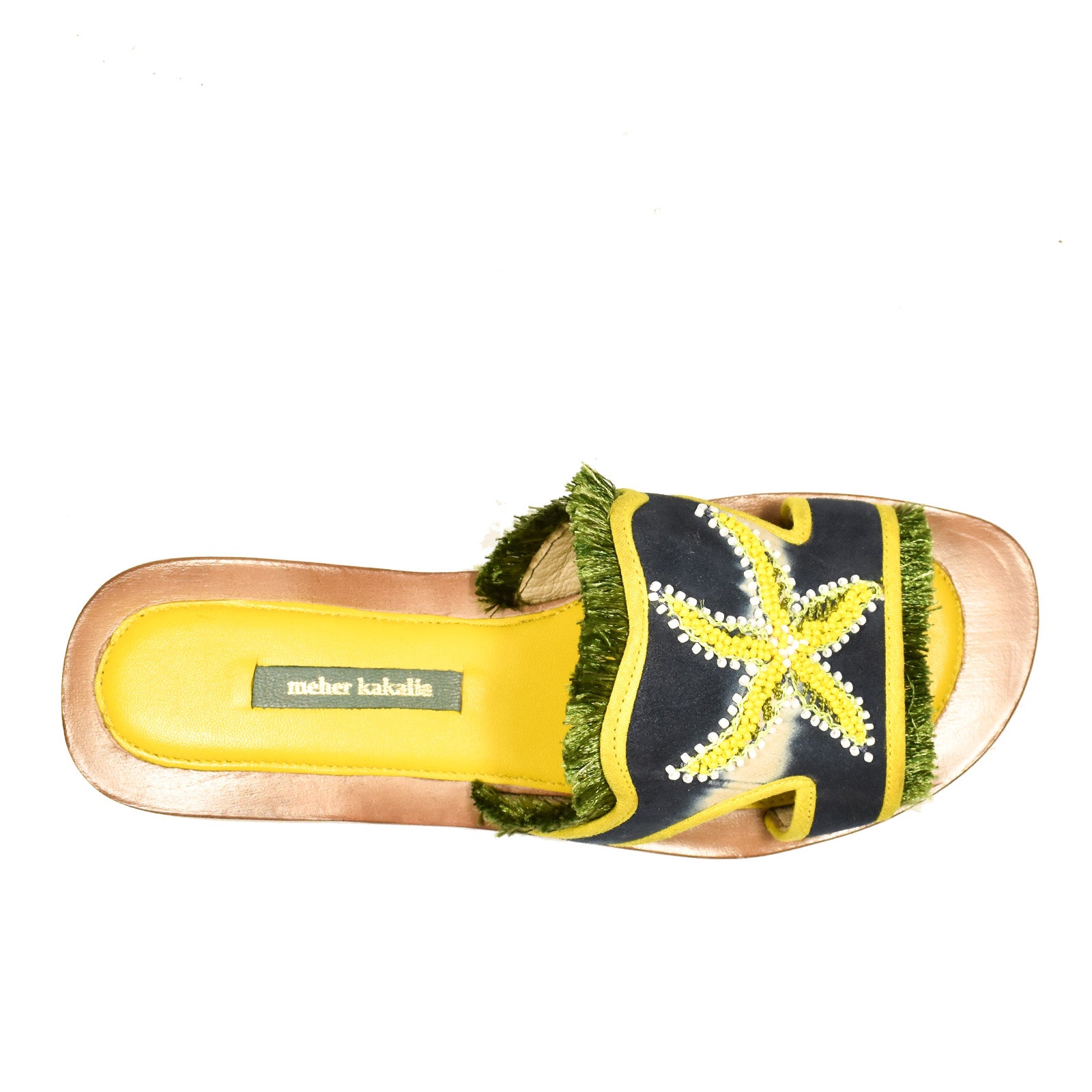 The Mazu Slide is a hand-embroidered leather sandal with a yellow sole, navy blue strap adorned with a yellow starfish motif, green fringe trim, and a visible Meher Kakalia label on the footbed—showcasing Meher Kakalia’s signature flair for sustainable footwear.