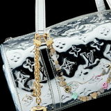 A silver Louis Vuitton handbag with embossed logos, adorned with the Heart Bag Charm—featuring a gold heart keychain, a colorful beaded accent, an elegant 14KT Gold Plate Chain, and a Martha Calvo Pendant—displayed against a black background.