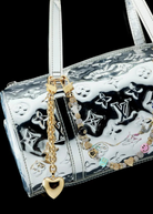 A silver Louis Vuitton handbag with embossed logos, adorned with the Heart Bag Charm—featuring a gold heart keychain, a colorful beaded accent, an elegant 14KT Gold Plate Chain, and a Martha Calvo Pendant—displayed against a black background.
