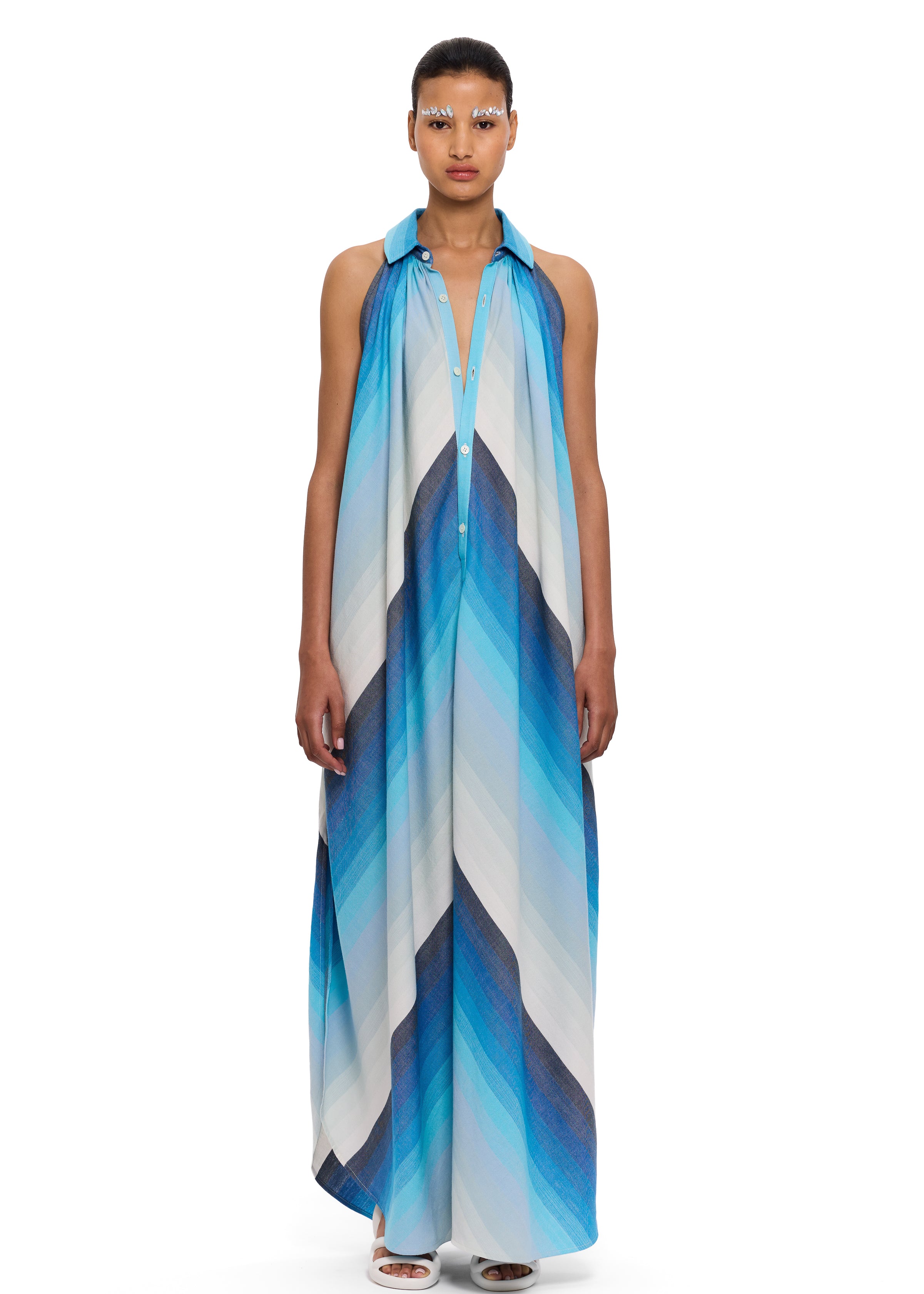 A person wearing The Halter Dress Small Point Collar, featuring a blue and white chevron pattern and expertly crafted from handwoven cotton that showcases Moroccan craftsmanship, stands facing forward against a plain white background.
