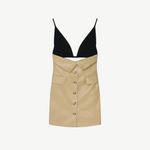 The Zyana Dress is a sleeveless style with a fabric-blocked design, showcasing a black deep V-neck top paired with a beige faux leather skirt featuring a button-down front and flap pockets. The dress is displayed against a plain background.