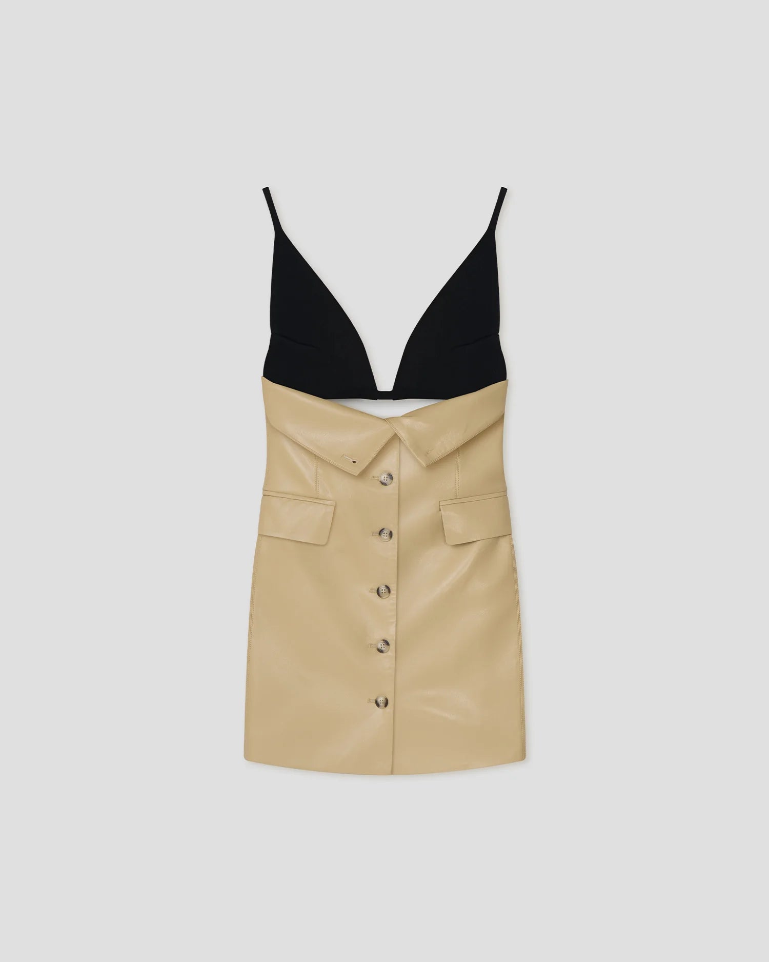 The Zyana Dress is a sleeveless style with a fabric-blocked design, showcasing a black deep V-neck top paired with a beige faux leather skirt featuring a button-down front and flap pockets. The dress is displayed against a plain background.