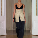 A model walks indoors wearing the Zyana Dress. The background features cream curtains and white paneled walls.