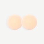 Two round, skin-toned Reusable Nippz self-adhesive nipple covers rest on a plain white background, slightly overlapping in the center. These washable covers offer a seamless and comfortable fit for everyday wear.