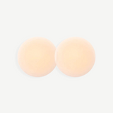 Two round, skin-toned Reusable Nippz self-adhesive nipple covers rest on a plain white background, slightly overlapping in the center. These washable covers offer a seamless and comfortable fit for everyday wear.