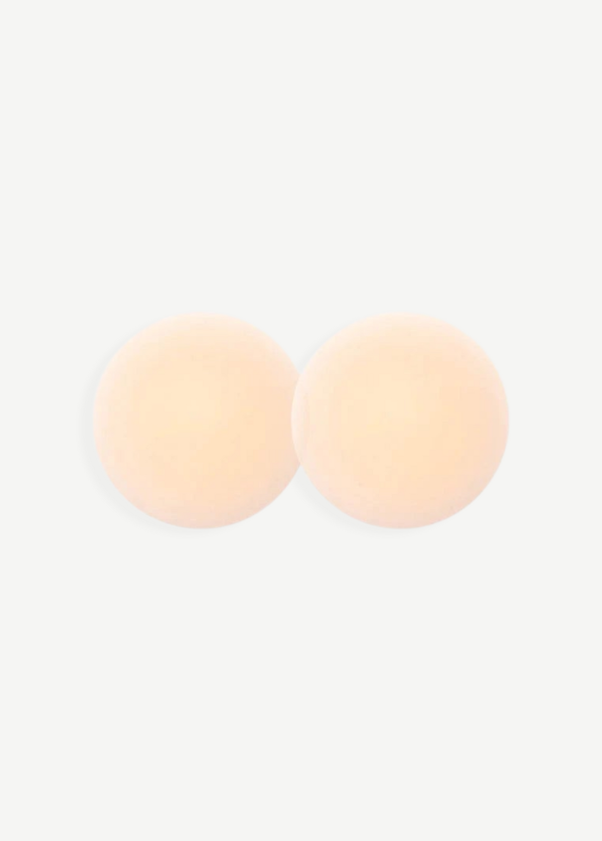 Two round, skin-toned Reusable Nippz self-adhesive nipple covers rest on a plain white background, slightly overlapping in the center. These washable covers offer a seamless and comfortable fit for everyday wear.