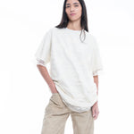 Wearing the Relaxed Fit T-Shirt with Lace Overlayer, a person with long, straight dark hair stands against a white background with one hand in their pocket, styled in beige wide-leg pants.