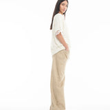 A woman with long brown hair stands sideways, wearing a Relaxed Fit T-Shirt with Lace Overlayer and wide-leg tan pants, hands in pockets, set against a plain white background.