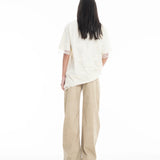 A person with long dark hair, wearing the Relaxed Fit T-Shirt with Lace Overlayer and wide-legged beige pants, stands facing away against a plain white background.