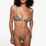 A woman wearing the Praia Bottom, a green patterned triangle bikini bottom with adjustable side ties, paired with sunglasses and a woven bucket hat, poses against a plain white background.