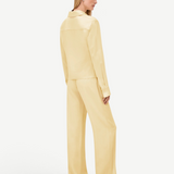 A person viewed from behind, wearing a pale yellow collared long-sleeve shirt and matching wide-leg Damian Pant for a polished style.