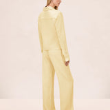 A person viewed from behind, wearing a pale yellow collared long-sleeve shirt and matching wide-leg Damian Pant for a polished style.