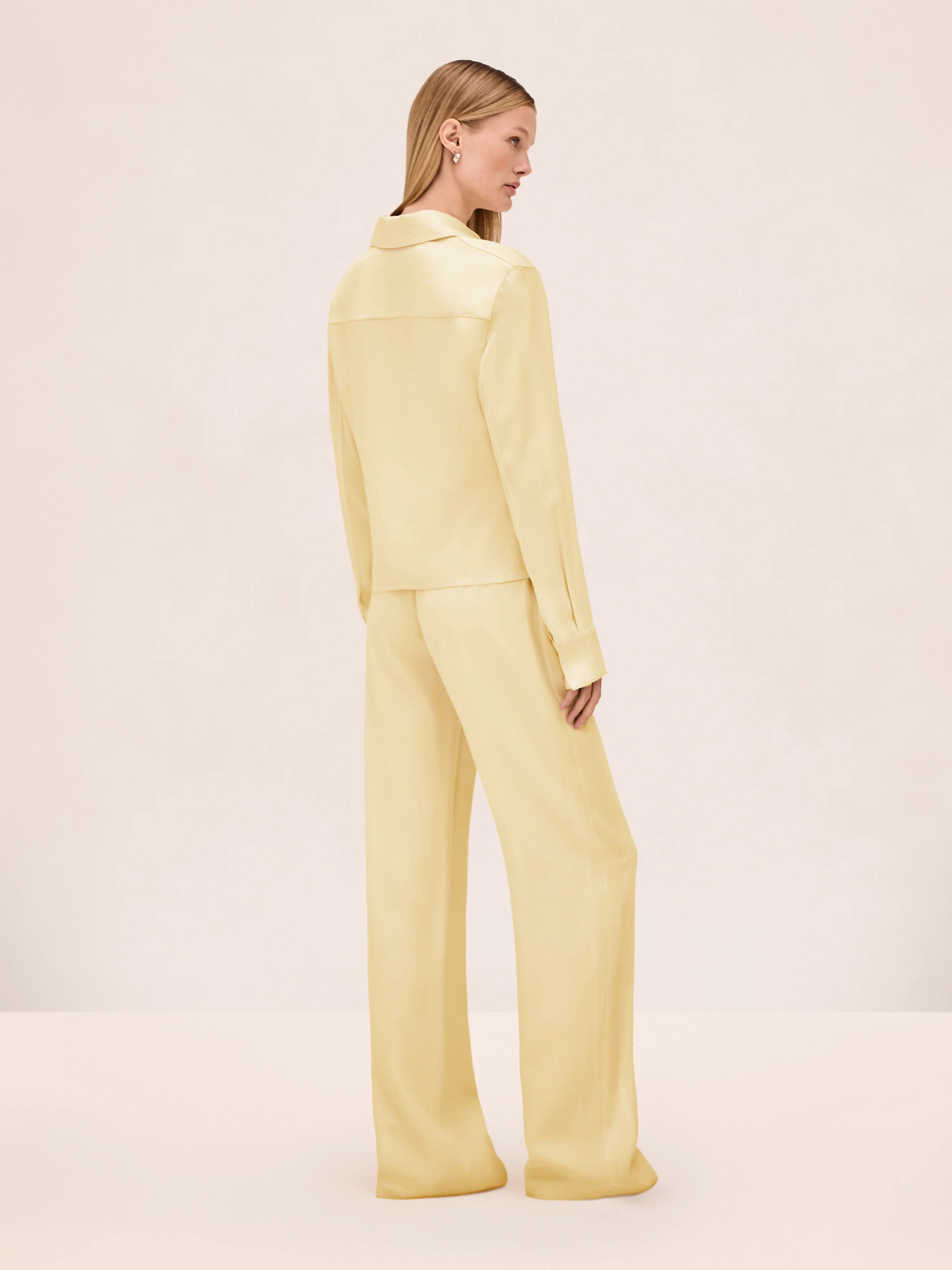 A person viewed from behind, wearing a pale yellow collared long-sleeve shirt and matching wide-leg Damian Pant for a polished style.