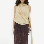 A model wearing a pale yellow Menorca top with an asymmetric silhouette and a floor-length brown lace skirt.