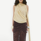 A model wearing a pale yellow Menorca top with an asymmetric silhouette and a floor-length brown lace skirt.