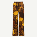 Veranera Pants: wide-leg silk twill trousers with a drawstring waist, featuring a brown and yellow floral print and overlapping script text.